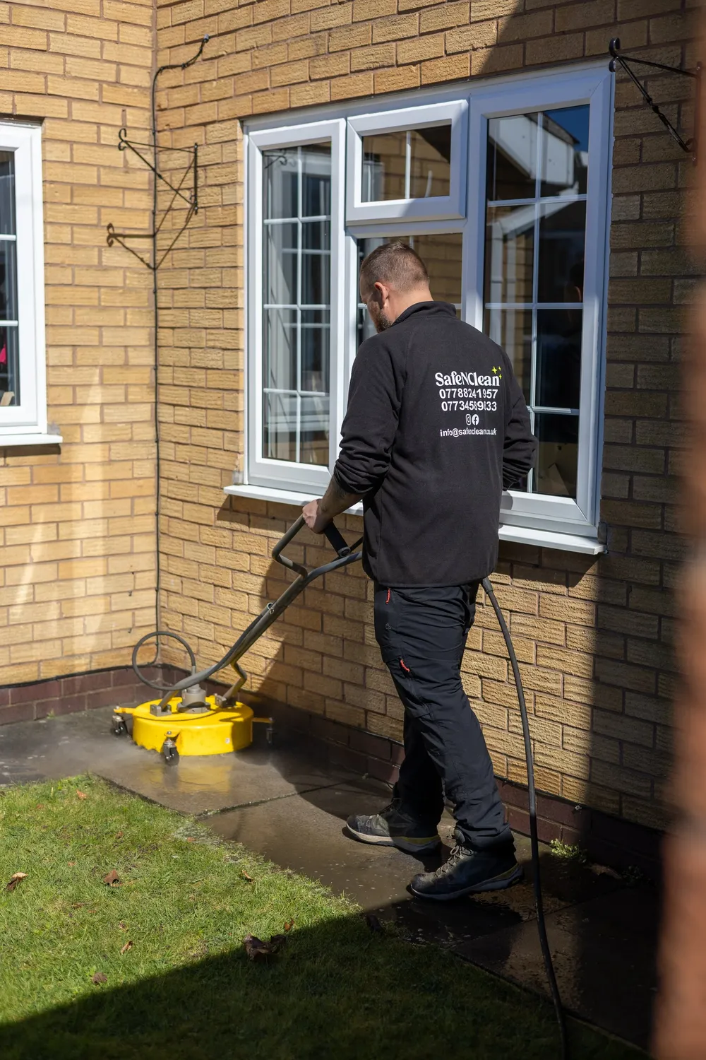 Rotary surface cleaner being used to pressure wash a patio next to a house wall