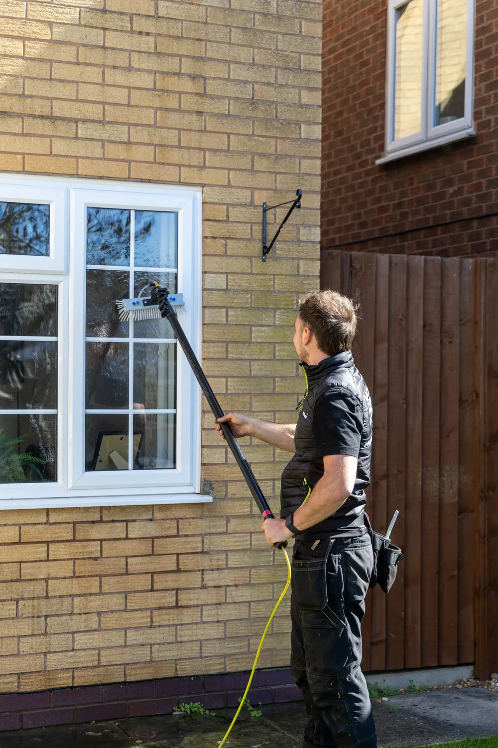 Window cleaner working on the front elevation of a brick house with a water-fed pole